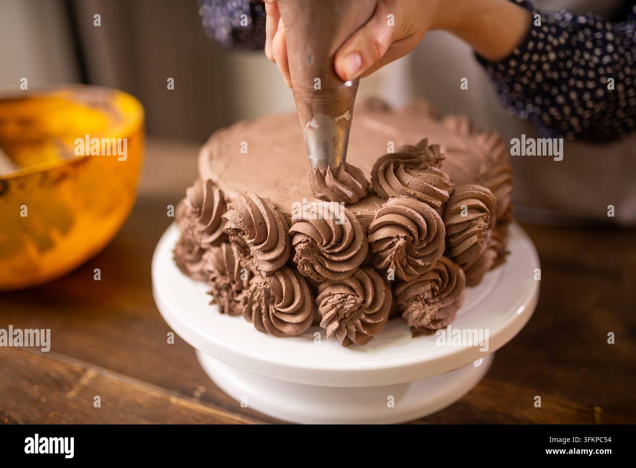 Handfertigung von Schokoladen-Buttercreme-Rosetten auf einem runden Schichttorten in einer gemütlichen Kücheneinrichtung Stockfoto