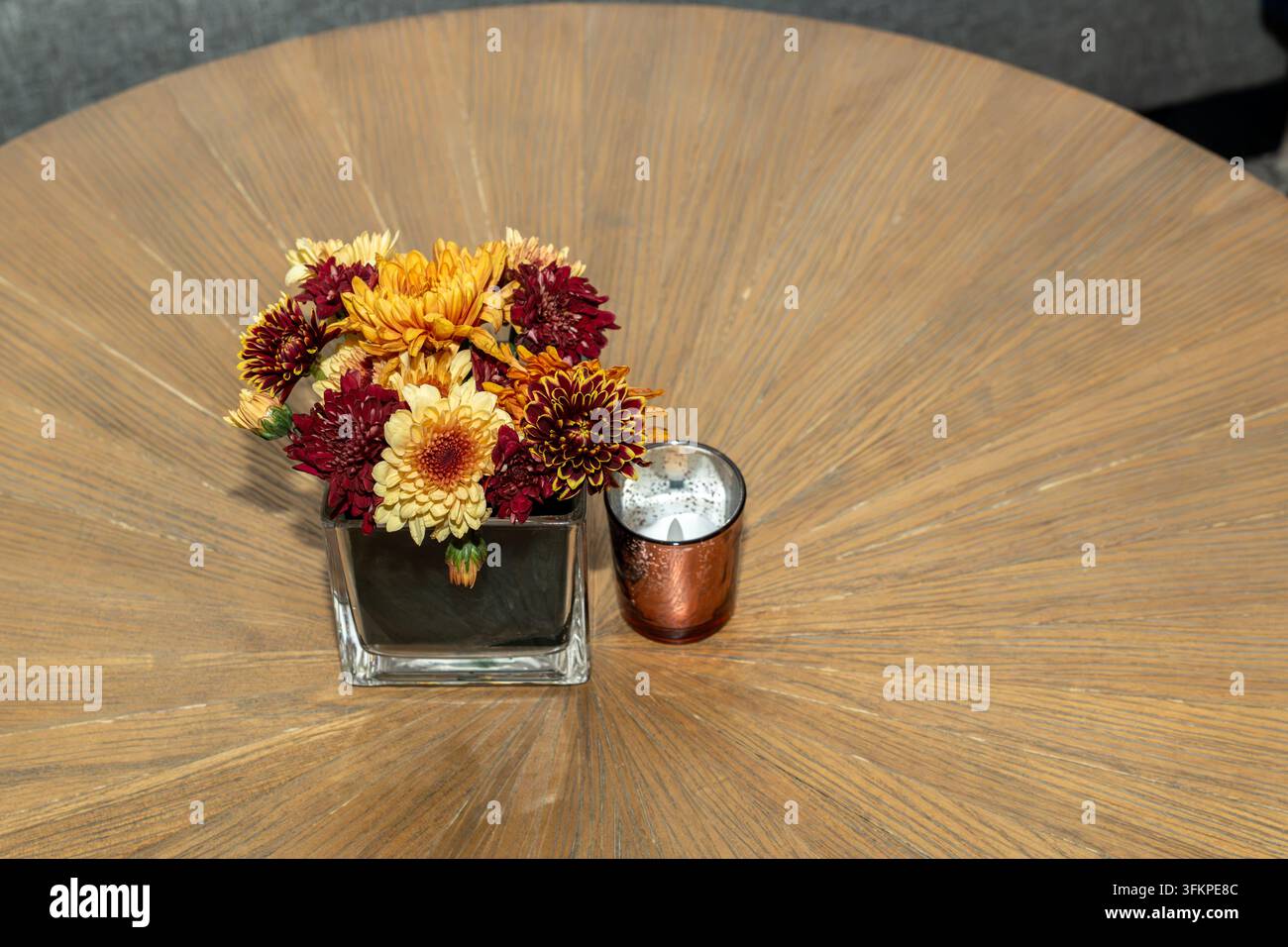 Holztisch dekoriert mit einem kleinen Strauß orangefarbener Blumen und einer Kerze, gemütliche Essatmosphäre, warmes Herbstdekor und natürliches Innenraumkonzept Stockfoto