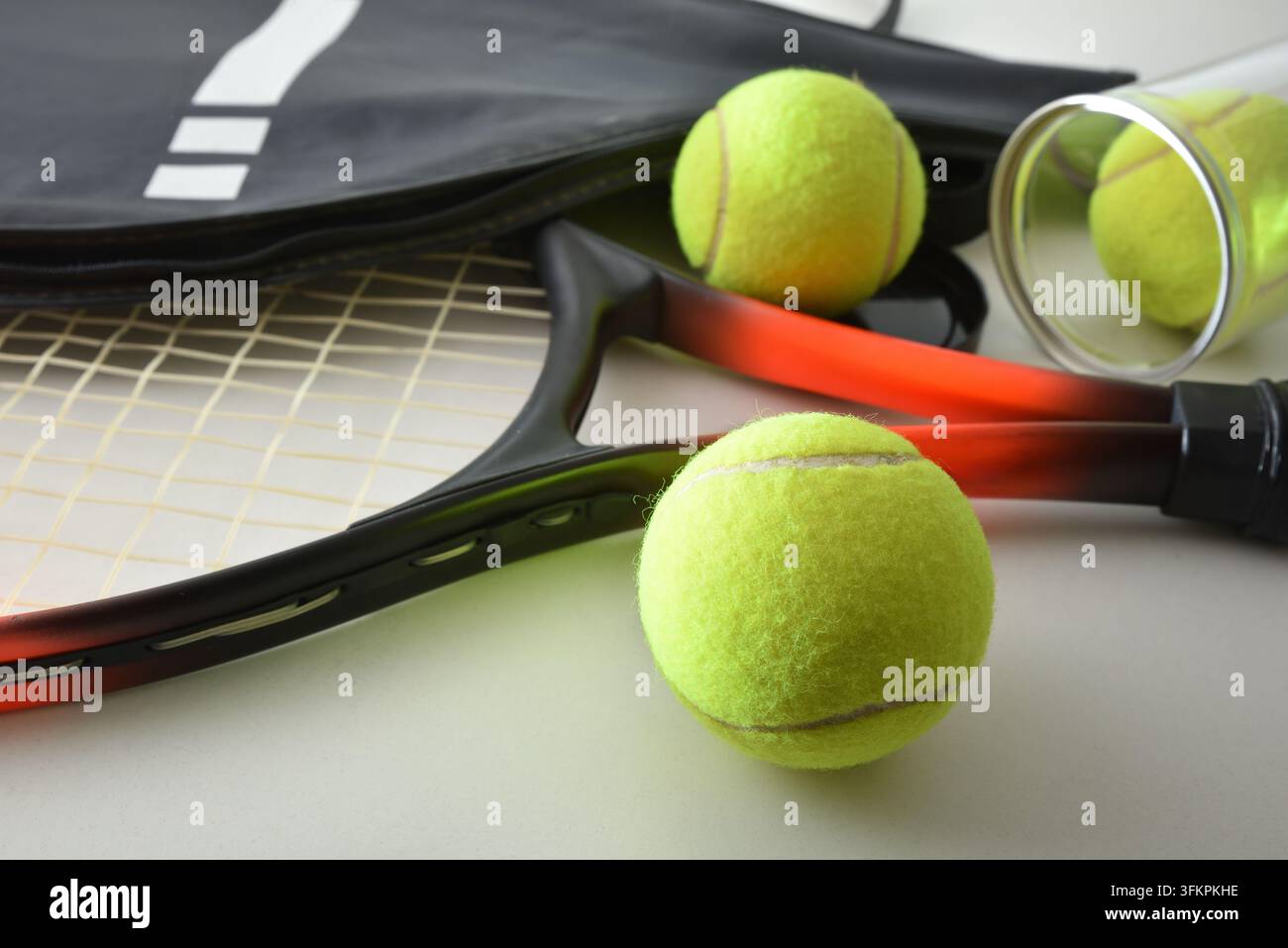 Tennisschläger, gelbe Bälle, eine schwarze Ausrüstungstasche und eine durchsichtige Ballröhre auf einem Tisch arrangiert, die ein detailliertes Stillleben mit Sportausrüstung bilden. Stockfoto