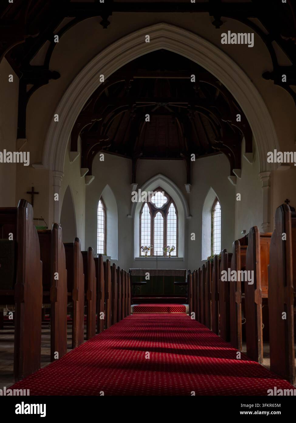 20. September 2026, Loweswater, Vereinigtes Königreich. Sonnenlicht strömt durch die gewölbten Fenster einer historischen Kirche und erhellt den roten Teppich, der führt Stockfoto