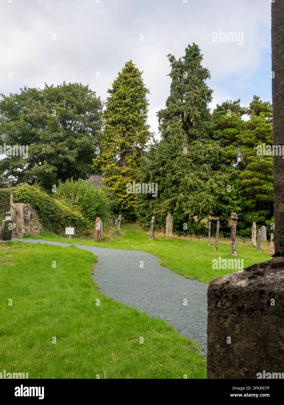 20. September 2026, Loweswater, Vereinigtes Königreich. Ein gewundener Kiesweg führt durch einen ruhigen Friedhof mit verwitterten Grabsteinen und üppigem grünem Gras Stockfoto