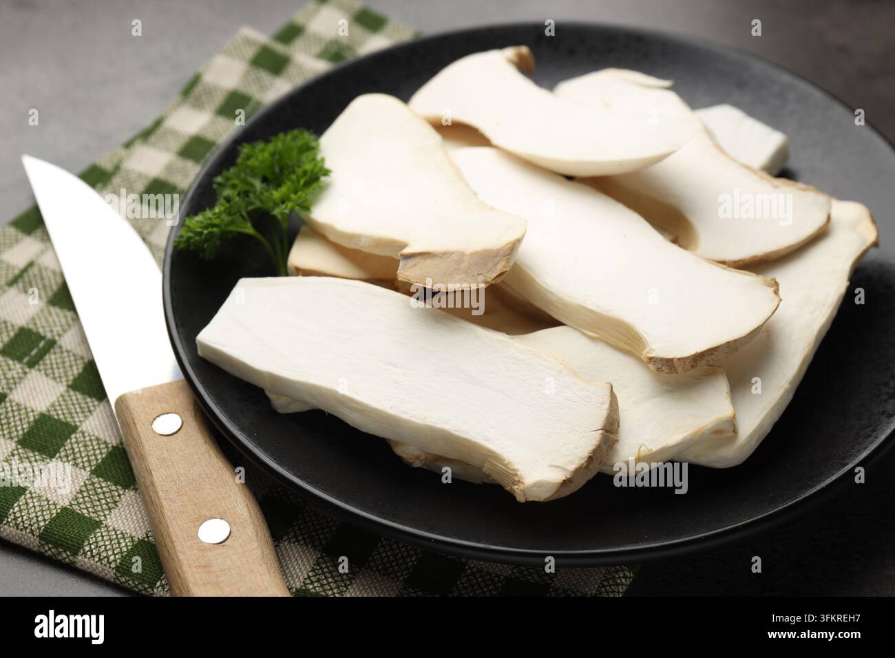 Frische Austernpilze mit Petersilie und Messer auf grauem Tisch, Nahaufnahme Stockfoto
