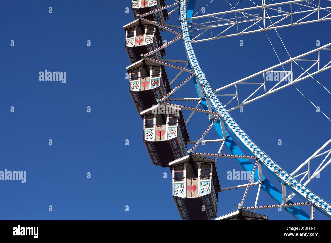 Niedrige diagonale Ansicht von traditionellen hölzernen Riesenradkabinen vor einem blauen Himmel auf dem berühmten Münchner Wiesn, Bayern Deutschland, Kopierraum links. Stockfoto