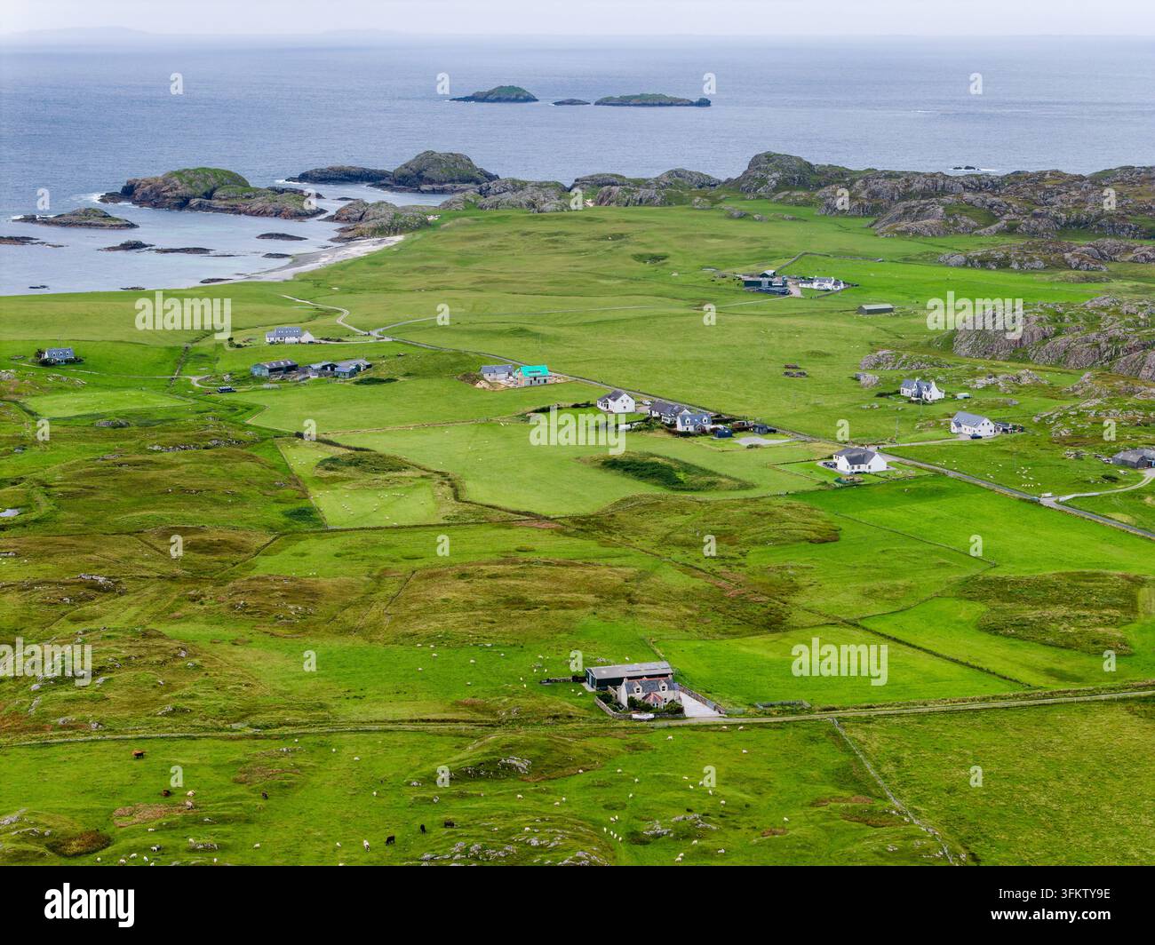 Ländliche Insellandschaft auf Iona, Schottland, verstreute weiße Häuschen über grüne Felder, die zu felsigen Küstenlinien und kleinen Küsteninseln führen, Luftaufnahme Stockfoto