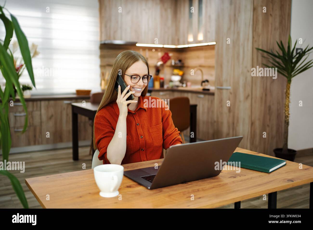 Frau, die multitaskingt und von zu Hause aus remote mit Laptop und Telefon arbeitet Stockfoto