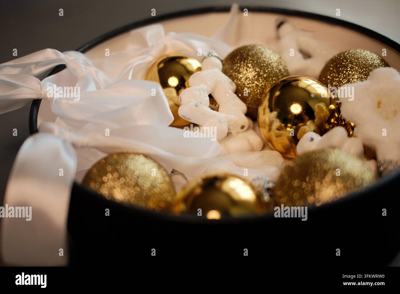 Goldene Weihnachtskugeln und weiße Schneeflockenornamente, die in einer dekorativen Schale arrangiert sind, schaffen ein luxuriöses festliches Tafelaufsatz für das Feierinterieur Stockfoto