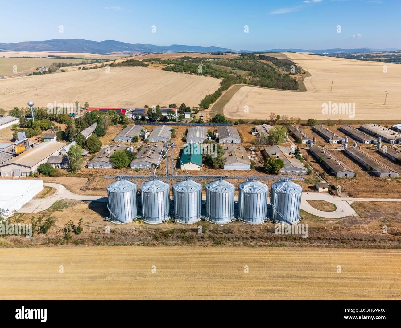 Luftaufnahme von Getreidesilos und Futtermittelanlagen in Paszto, Nograd County, Nordungarn, umgeben von Ackerland, Weizenfeldern und ländlichen Hügeln i Stockfoto