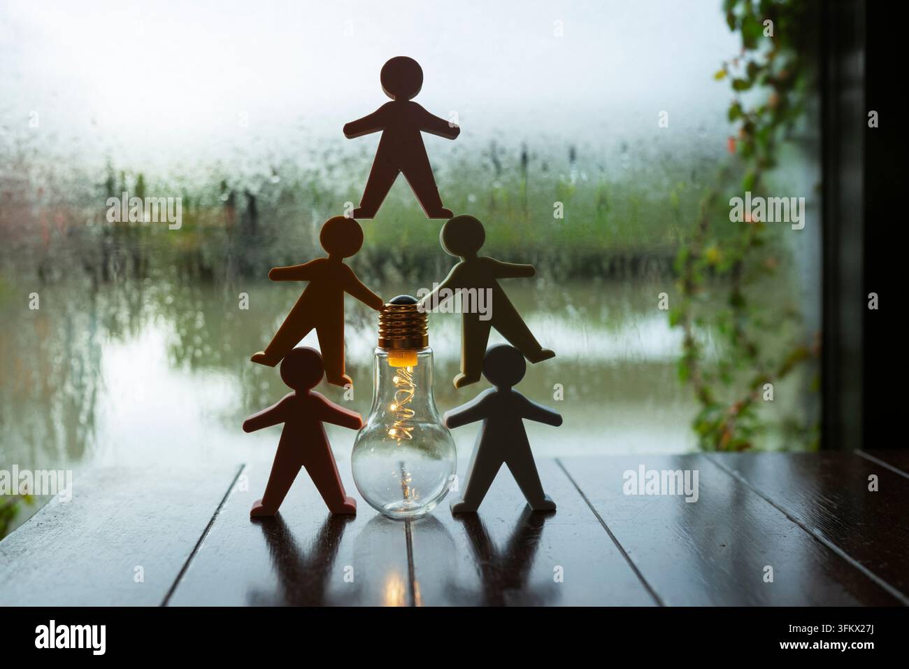 Team-Innovation und kreatives Brainstorming-Konzept, menschliche Figuren in einer Pyramide um eine leuchtende Glühbirne auf dem Tisch gestapelt, die kollaborative Idee symbolisierend Stockfoto