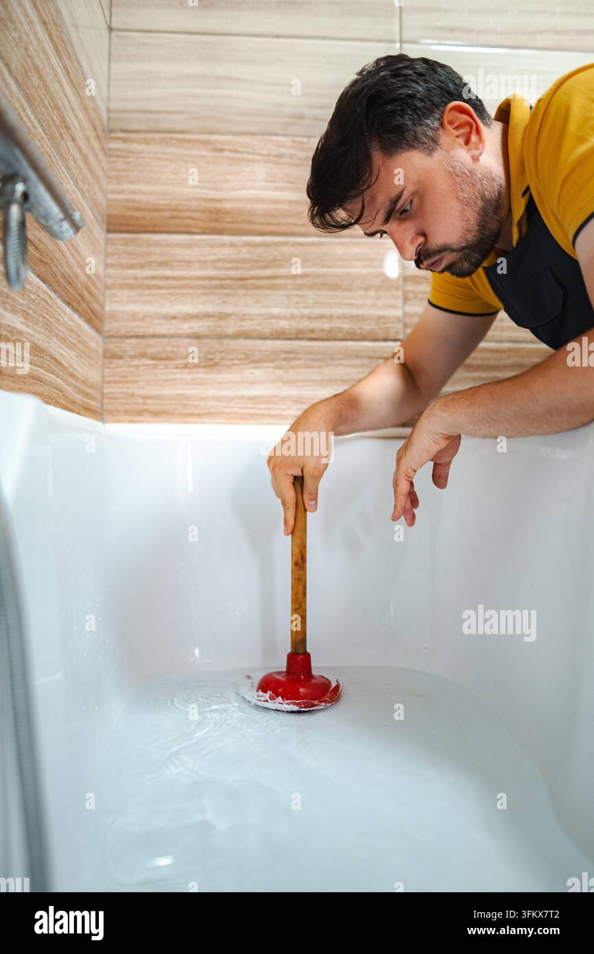Handwerker stößt verstopften Badewannenabfluss und behebt ein Klempnerproblem Stockfoto