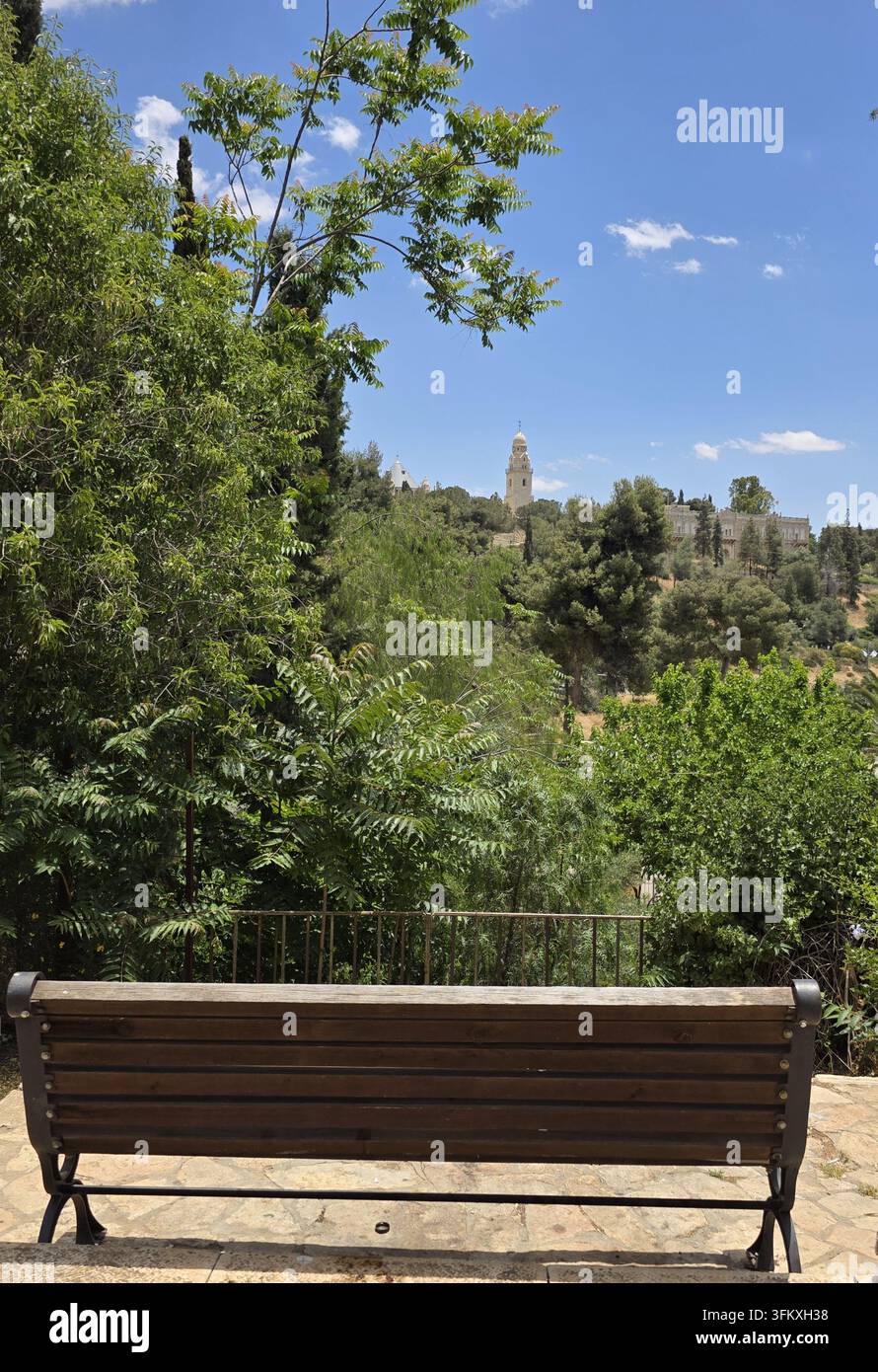 Holzbank in einem grünen Park mit einem malerischen Blick auf die Abtei der Entschlafung auf dem Zion in Jerusalem, Israel. Stockfoto