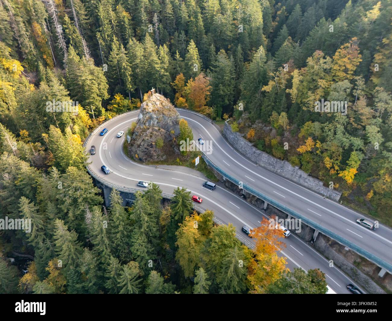 Aus der Vogelperspektive einer Haarkurve auf der Bergstraße mit einem Kreuz auf dem Felsen im Herbst Stockfoto
