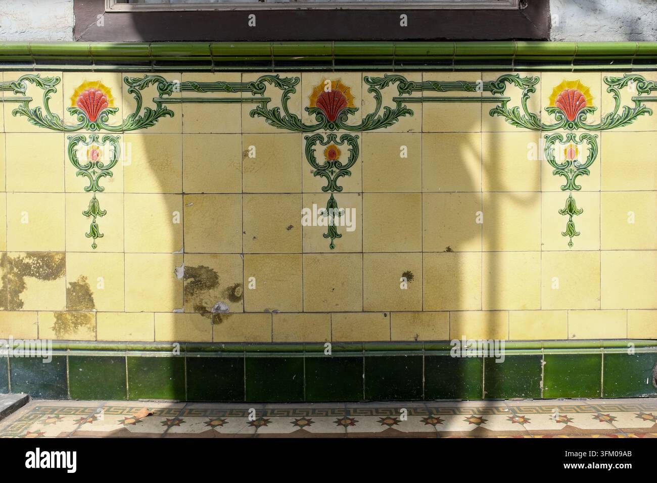 Vintage-dekorative Keramikwandfliesen mit sich wiederholenden roten Blumenmotiven und grünen ornamentalen Schnörkelverzierungen an einem historischen Geschäftshaus in George Town, Penang Stockfoto