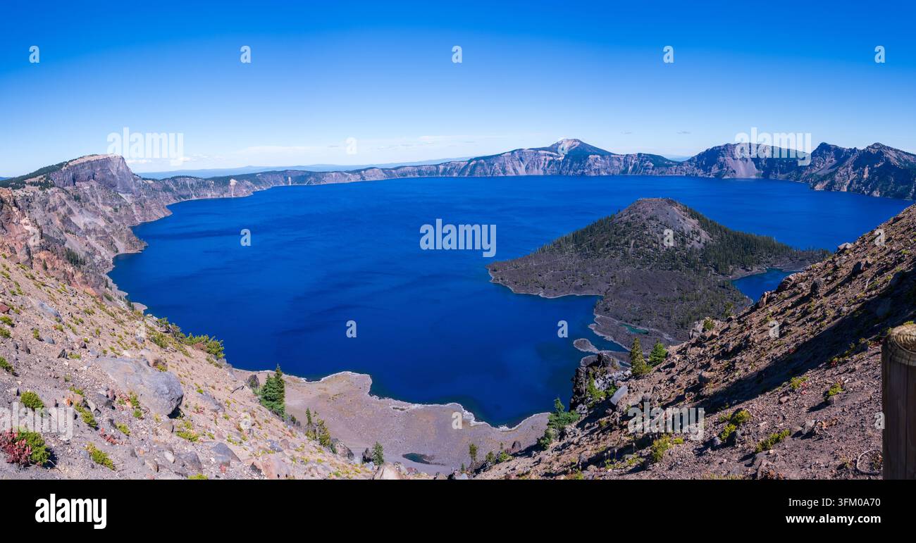Panoramic view of Crater Lake in Oregon, eine tiefe blaue vulkanische Caldera umgeben von rauem Gelände und klarem Himmel. Stockfoto