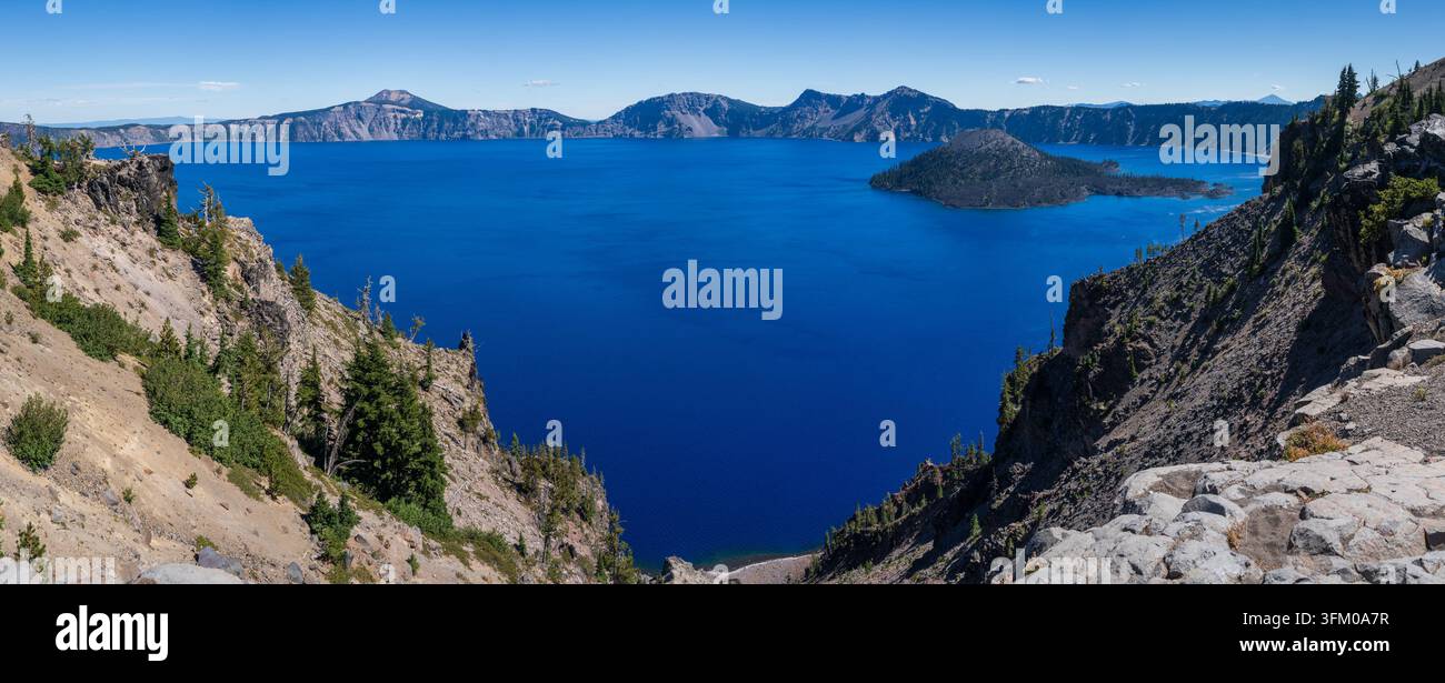 Blick auf den tiefblauen vulkanischen Crater Lake in Oregon von Merriam Point aus, der steile felsige Ufer und entfernte Berge zeigt Stockfoto