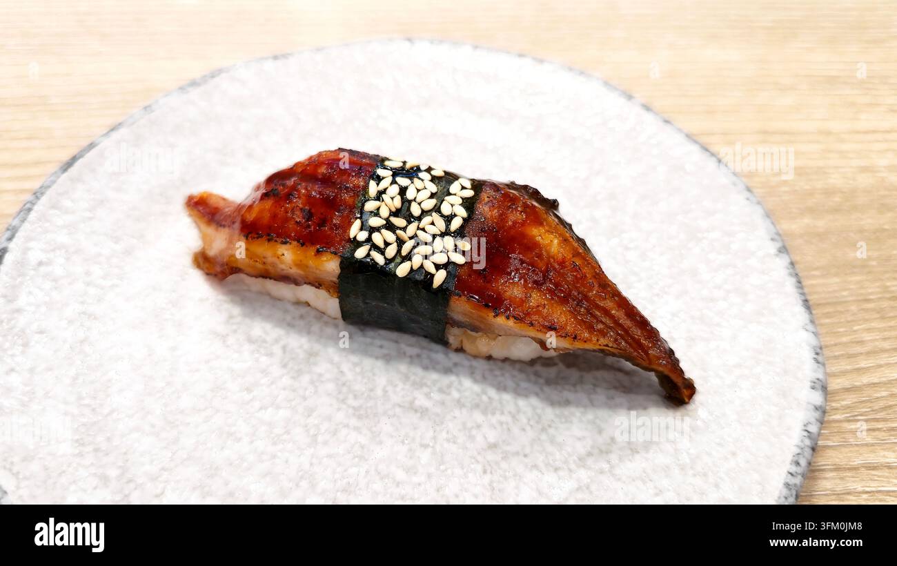 Japanischer Unagi Nigiri Sushi mit gegrilltem, glasiertem Aal, gewickelt in Nori und mit Sesamsamen belegt, serviert auf einem Keramikteller in einem Restaurant. - Smartphone-aufgenommenes Stockfoto