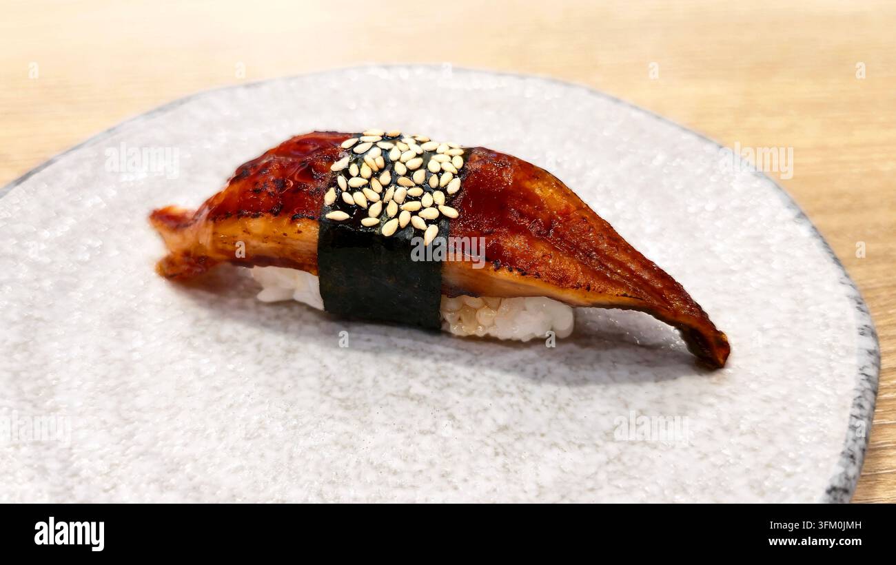 Japanischer Unagi Nigiri Sushi mit gegrilltem, glasiertem Aal, gewickelt in Nori und mit Sesamsamen belegt, serviert auf einem Keramikteller in einem Restaurant. - Smartphone-aufgenommenes Stockfoto