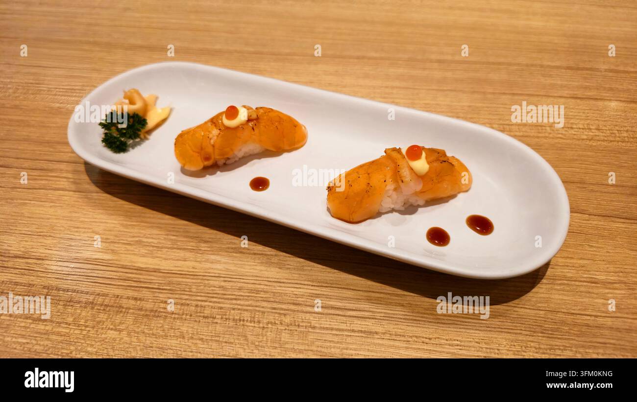 Gebratener Lachs-Nigiri-Sushi mit cremiger Sauce und Lachs-Rogen, serviert auf einem weißen Keramikteller mit flacher Schärfentiefe in einem japanischen Restaurant - Smartphone-aufgenommenes Stockfoto