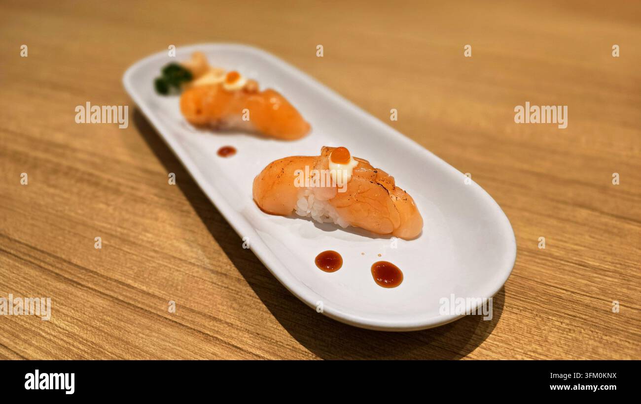 Gebratener Lachs-Nigiri-Sushi mit cremiger Sauce und Lachs-Rogen, serviert auf einem weißen Keramikteller mit flacher Schärfentiefe in einem japanischen Restaurant - Smartphone-aufgenommenes Stockfoto