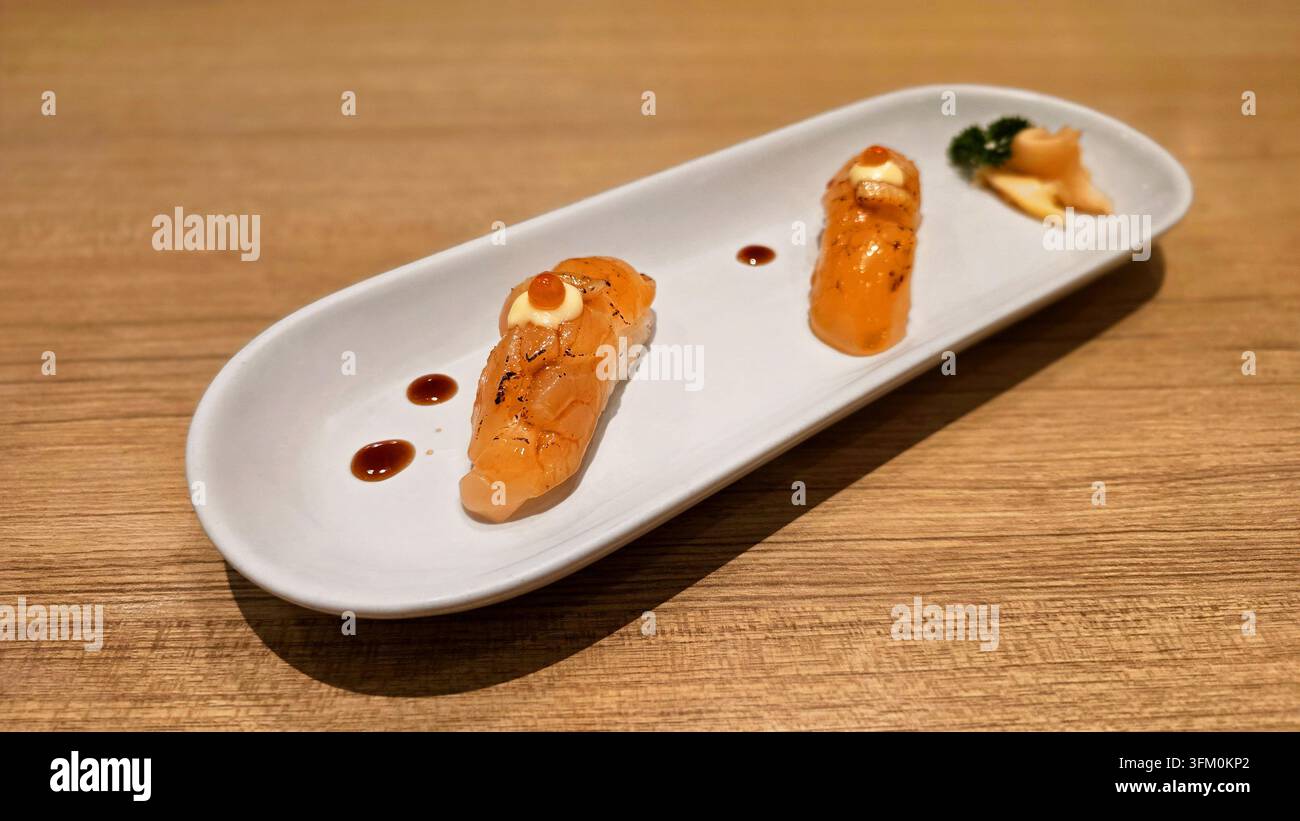 Gebratener Lachs-Nigiri-Sushi mit cremiger Sauce und Lachs-Rogen, serviert auf einem weißen Keramikteller mit flacher Schärfentiefe in einem japanischen Restaurant - Smartphone-aufgenommenes Stockfoto