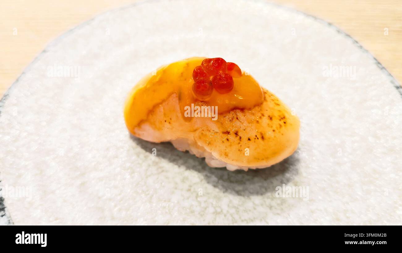 Gebratener Jakobsmuschel-Nigiri-Sushi, überzogen mit cremiger würziger Sauce und hellem Lachs-Rogen, serviert auf einem Keramikteller als japanischer Meeresfrüchte-Delikatess - Smartphone-aufgenommenes Stockfoto