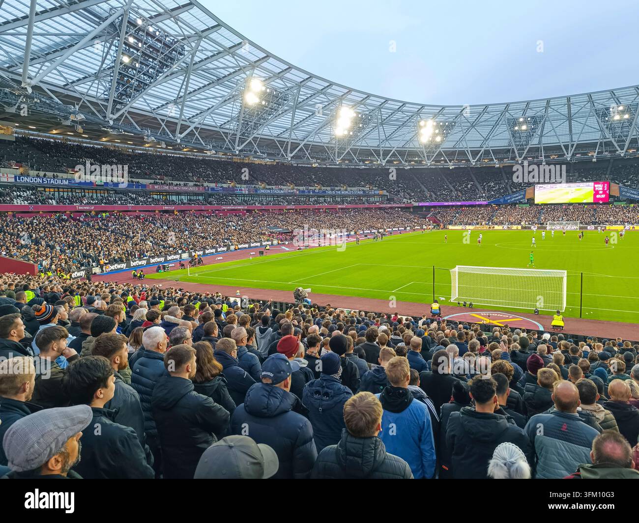 Eine große Menge leidenschaftlicher Fußballfans füllt die Tribünen im London Stadium während eines aufregenden Abendspiels unter den hellen Arena-Lichtern. London Stockfoto