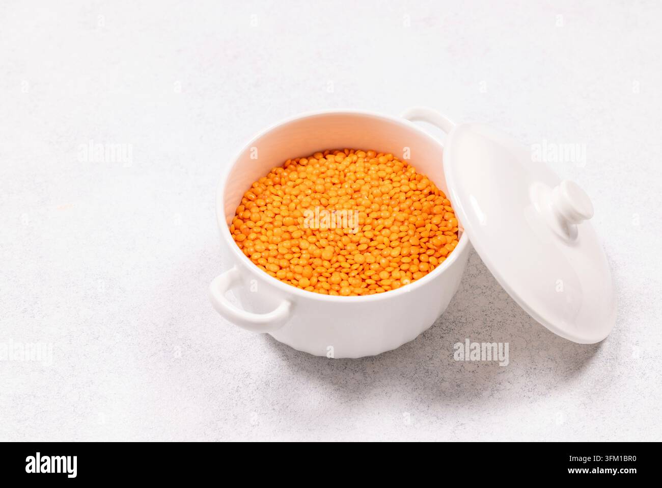Rote Linsen füllen einen weißen Keramiktopf mit Deckel und präsentieren Zutaten für gesunde Superfood-, Vegan- und Vegetarier-Kochoptionen, wobei der Nährwert betont wird Stockfoto