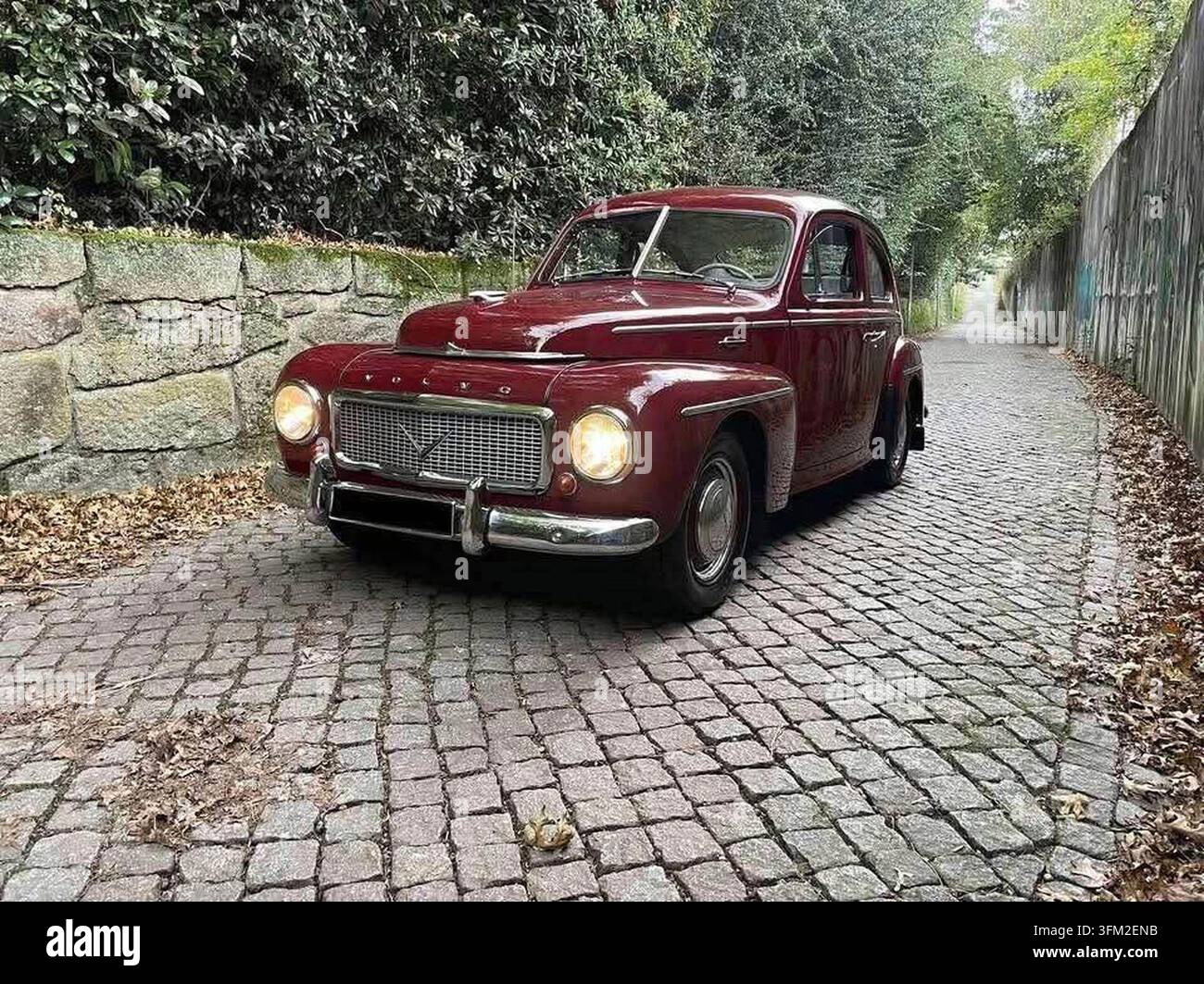 Klassischer burgunderroter Volvo PV444, der auf einer Kopfsteinpflasterstraße geparkt ist und seinen Vintage-Charme und seine Eleganz zur Schau stellt Stockfoto