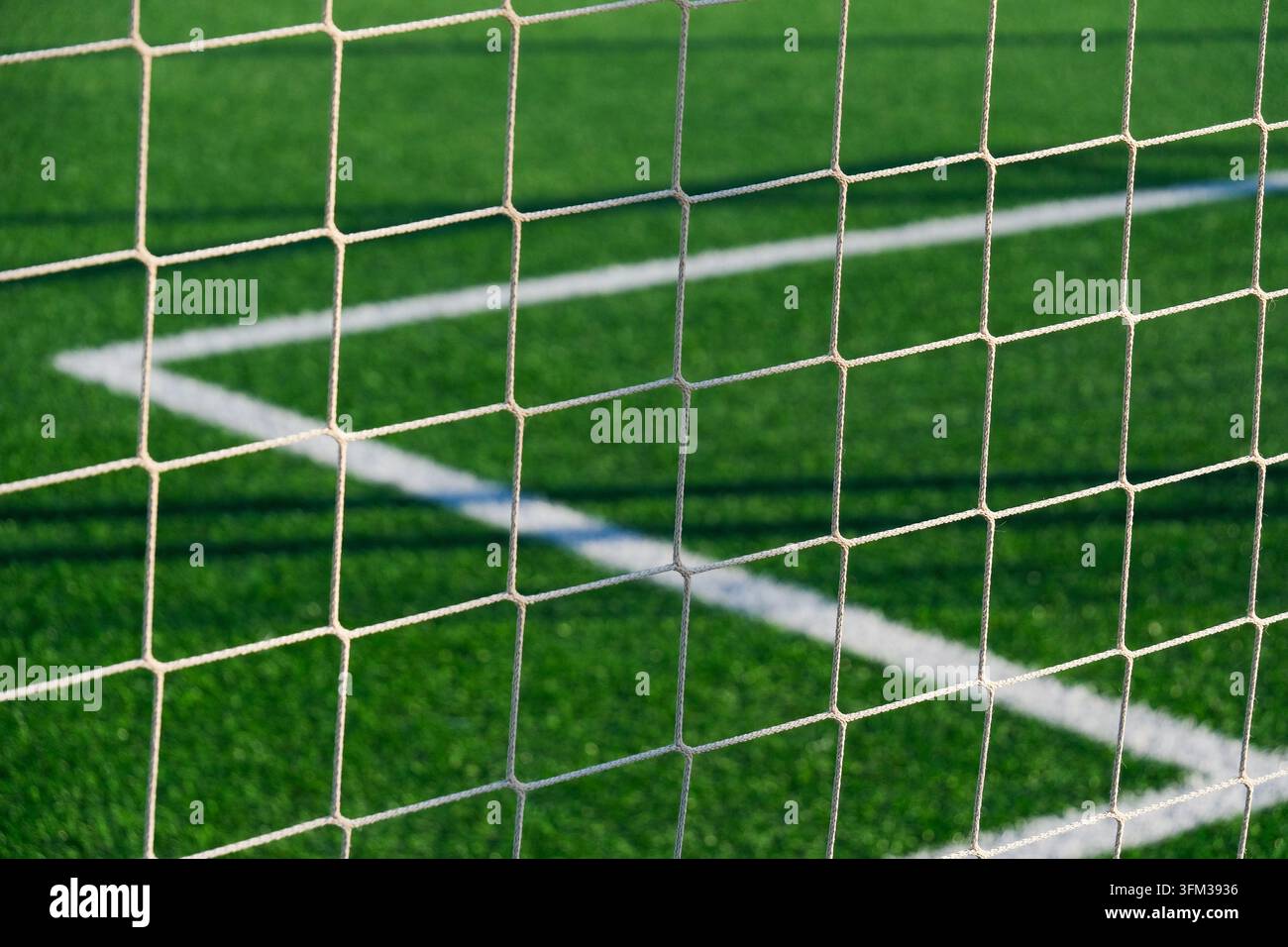 Weißes Fußballspannnetz in Nahaufnahme vor lebhaft grünem Kunstrasen mit sich kreuzenden Feldmarkierungen und geometrischem Maschenmuster im Außensportbereich Stockfoto