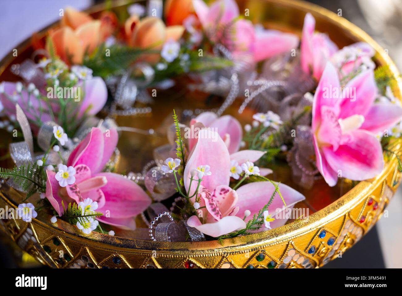 Eine kunstvolle goldene Schale gefüllt mit einem rosa Orchideenblumenarrangement und zarten weißen Blüten details, die ein elegantes dekoratives Tafelaufsatz für Feierlichkeiten schaffen Stockfoto