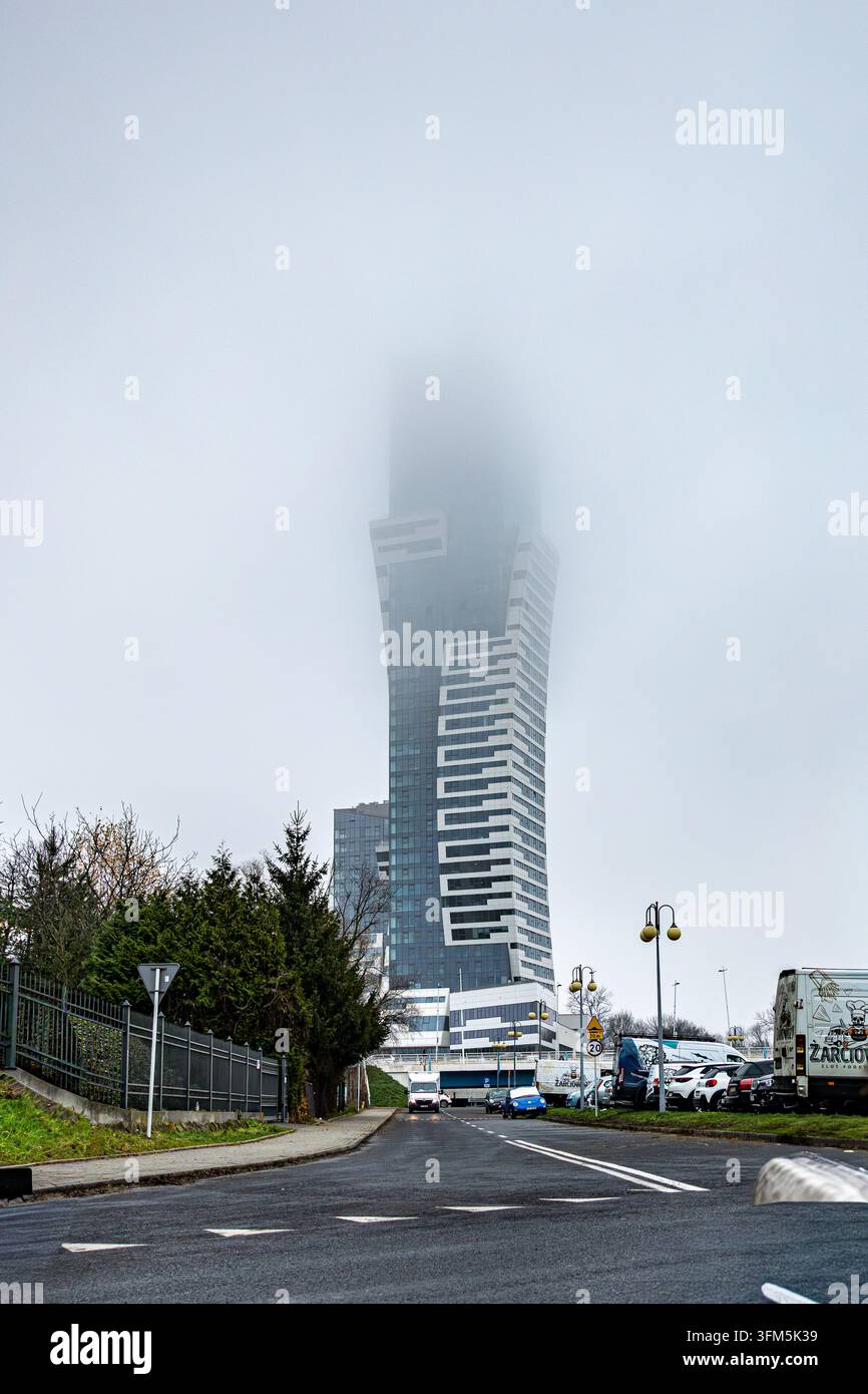 Moderner Hochhausturm, der durch dichten Nebel über einer Straße in Rzeszow aufsteigt Stockfoto