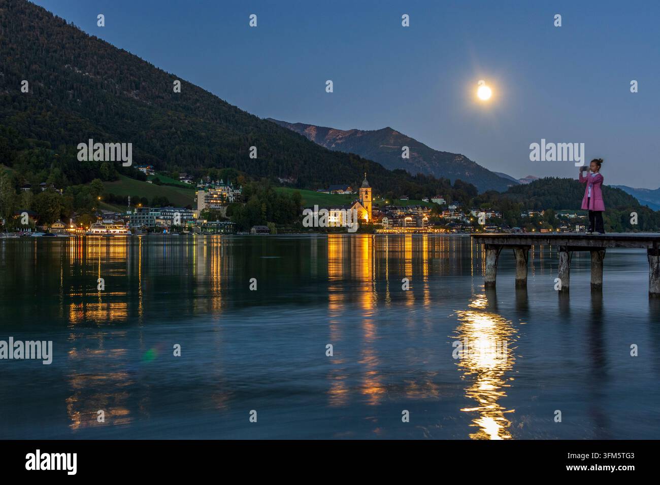 St. Wolfgang im Salzkammergut: Wolfgangsee, Stadt und Kirche St. Wolfgang, Vollmond, Frau auf Bootssteg, die in Salzka Fotos macht Stockfoto