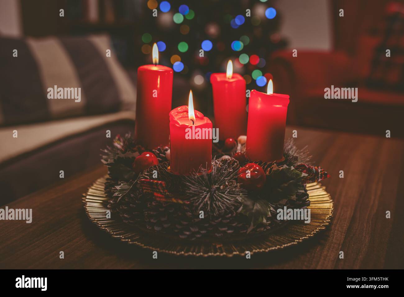 Vier brennende rote Adventskerzen, die auf einem dekorativen Kranzmitte aus Tannenzapfen, Beeren und Grünzeug angeordnet sind, auf einem Holztisch platziert mit Weihnachten Stockfoto