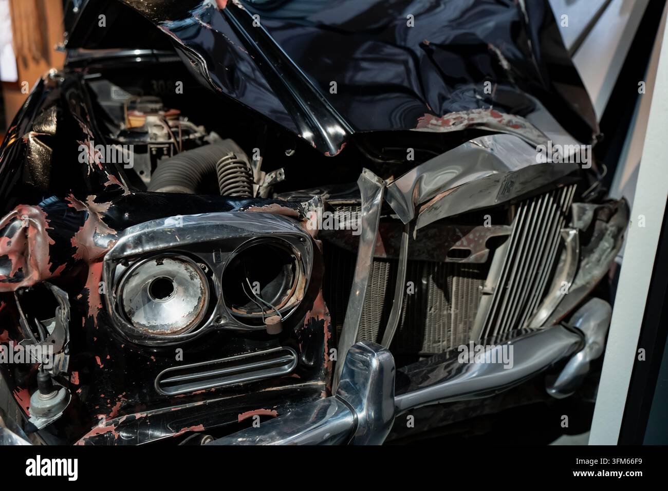 Beschädigte Vorderfront eines Oldtimers mit fehlenden Scheinwerfern, zerrissenen Paneelen, freiliegendem Kühler und verbogener Frontgrillierung, zur Unterstützung der Kollisionsbewertung, des Recyclings und an Stockfoto