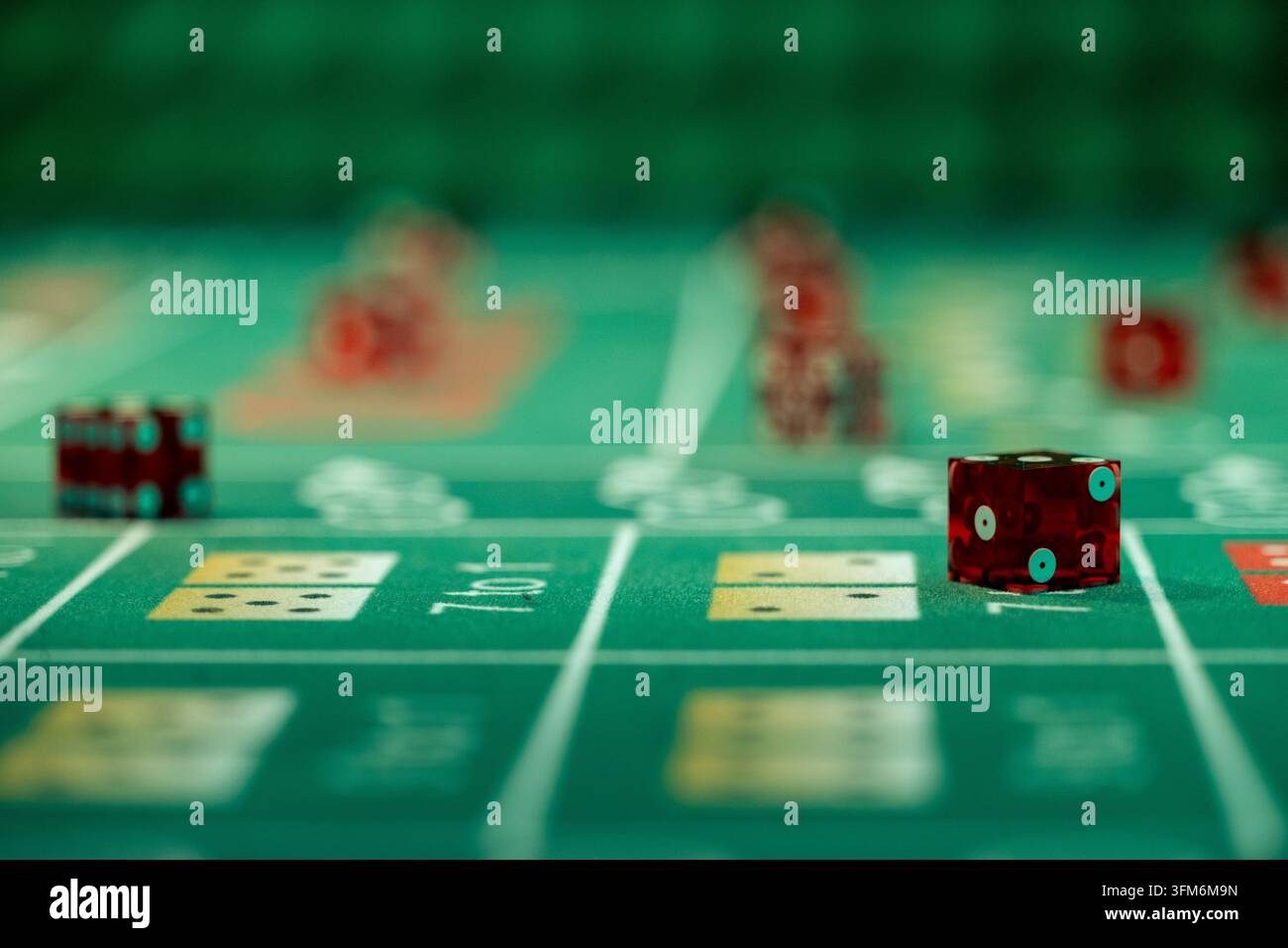 Rote Würfel, die über Auszahlungsfeldern auf einem grünen Craps-Tischlayout ruhen. Bild mit geringer Tiefenschärfe, zentriert auf den vorderen Würfel. Stockfoto