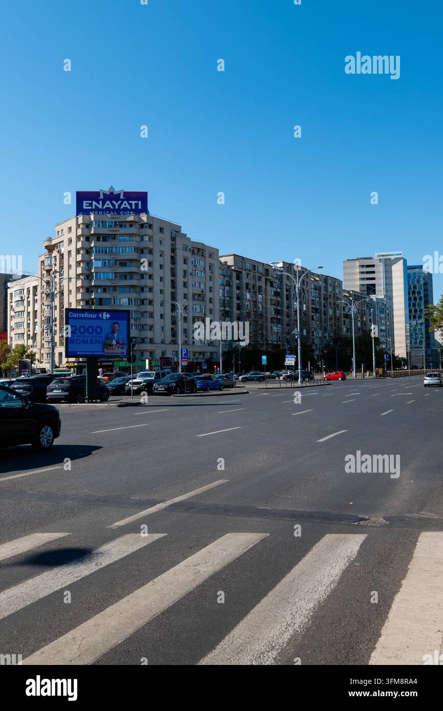 Straßensicht der Piata Victoriei in Bukarest mit Wohnblocks, einem Fußgängerüberweg, geparkten Autos und Werbetafeln auf den Dächern. Stockfoto