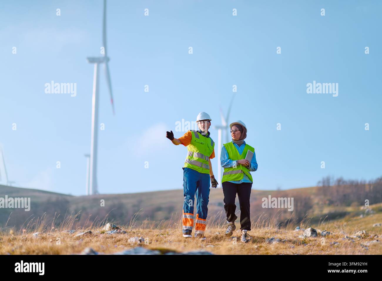 Ingenieure inspizieren Windpark im Freien und tragen Sicherheitswesten und Schutzhelme an einem erneuerbaren Energiestandort Stockfoto