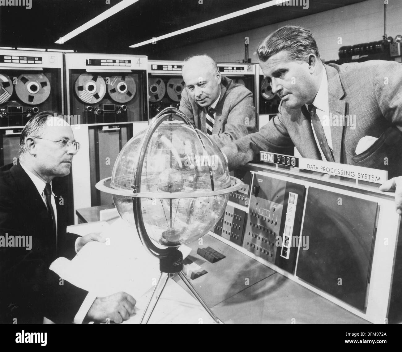 Eine Fotografie, die den deutsch-amerikanischen Luft- und Raumfahrtingenieur Wernher von Braun (1912–1977) und seine Kollegen George Mueller und Eberhard Rees zeigt, wie sie vor einem IBM 7090 Datenverarbeitungssystem im Marshall Space Flight Center einen Himmelsglobus untersuchen. Nach seiner Beteiligung am deutschen Raketenprogramm während des Zweiten Weltkriegs zog von Braun in die Vereinigten Staaten, wo er zu einer führenden Figur im amerikanischen Raumfahrtprogramm wurde. Als Direktor des Marshall Space Flight Center überwachte er die Entwicklung der Saturn-V-Rakete, die schließlich die Apollo-Mondmissionen ermöglichte. Ca. 1963. Stockfoto
