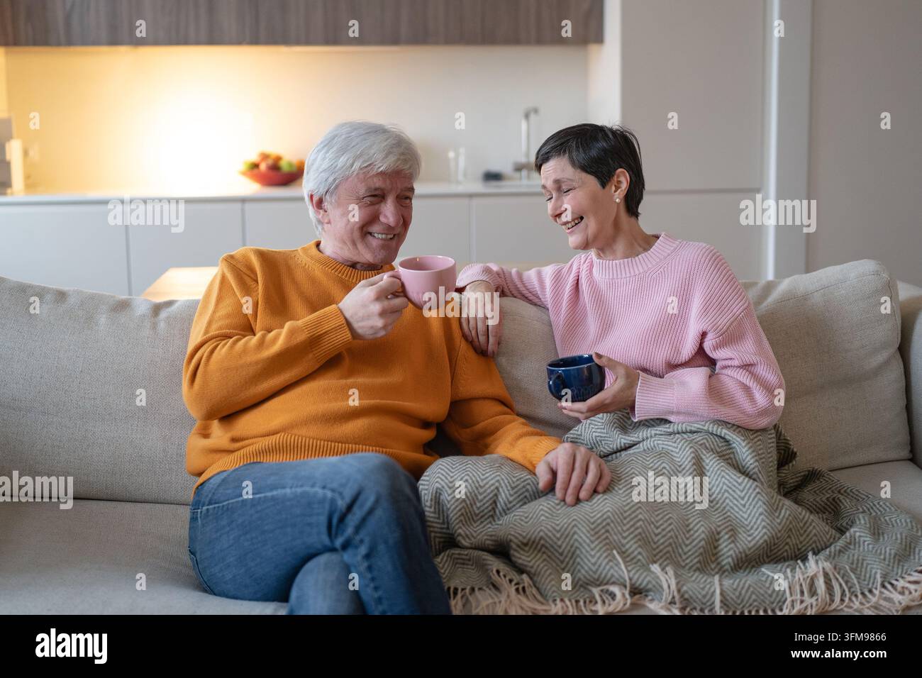 Glückliche Senioren-Ehepartner genießen Tee und Gespräche, entspannen zusammen auf einer bequemen Heimcouch Stockfoto