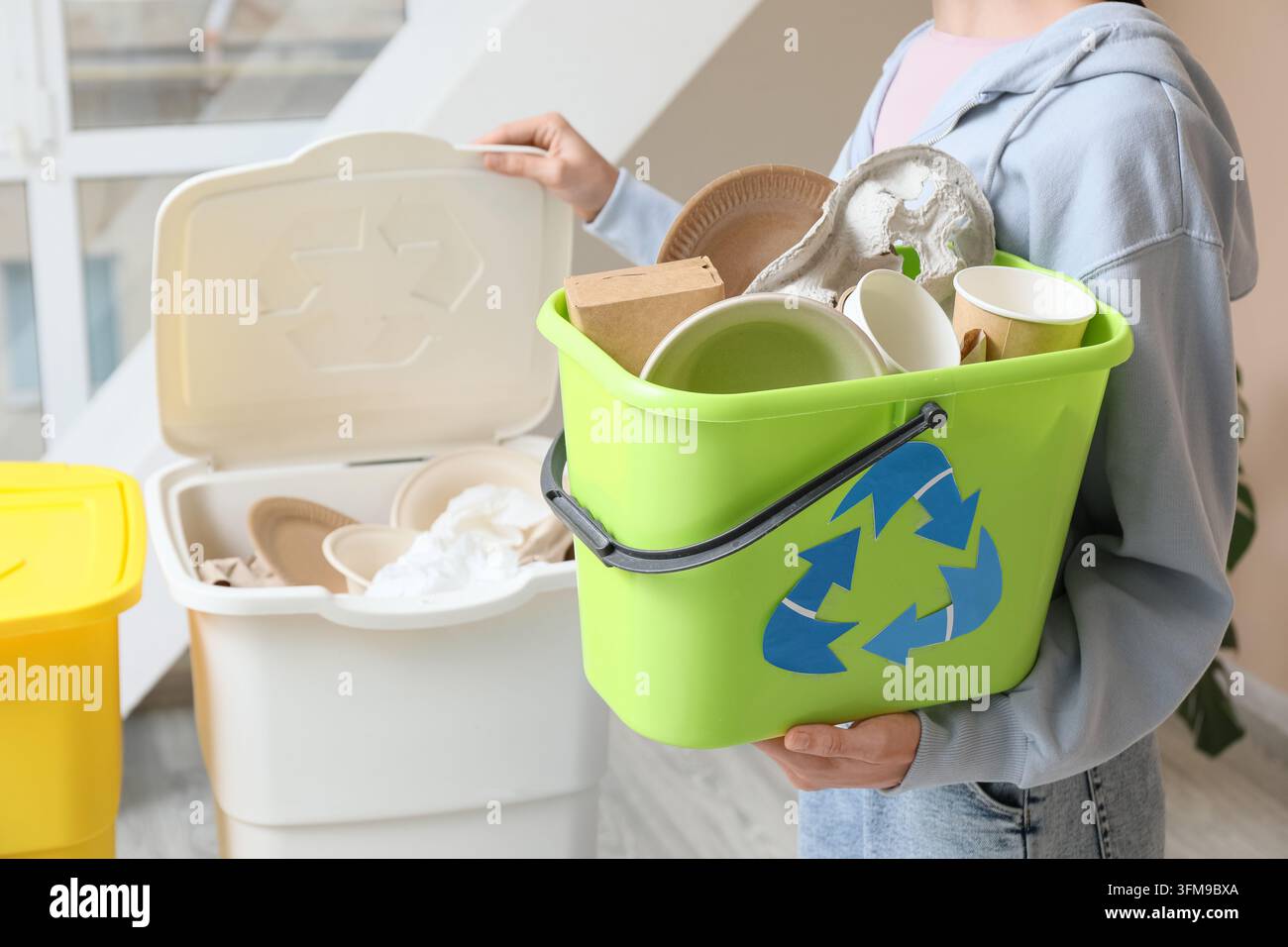 Nachhaltigkeit und Abfallmanagement, Person sortiert recycelbares Papier und Kartonverpackungen in einen grünen Behälter zur Umweltbewahrung zu Hause Stockfoto