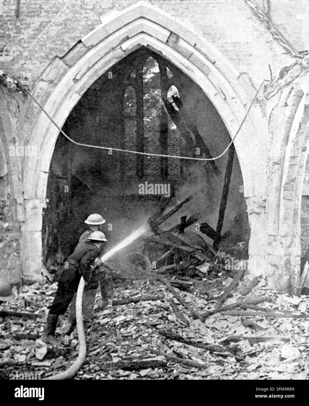 Ein Foto, das britische Feuerwehrleute zeigt, die die glimmenden Überreste von Dachbalken in einer Kirche nach einem deutschen Luftangriff löschen. In den frühen Phasen des Zweiten Weltkriegs zielten deutsche Luftangriffe auf verschiedene britische Infrastrukturen und zivile Gebäude als Vorläufer der anhaltenden Bombenkampagne, die als der Blitz bekannt ist. Die Feuerwehrdienste, einschließlich des Auxiliary Fire Service, spielten eine entscheidende Rolle bei der Löschung von Bränden, die durch Brandbomben verursacht wurden, um historische Wahrzeichen und städtische Zentren zu schützen. Die Szene zeigt zwei Männer in Uniform, die einen Wasserschlauch auf verkohltes Trümmerwerk unter dem Dach richten Stockfoto