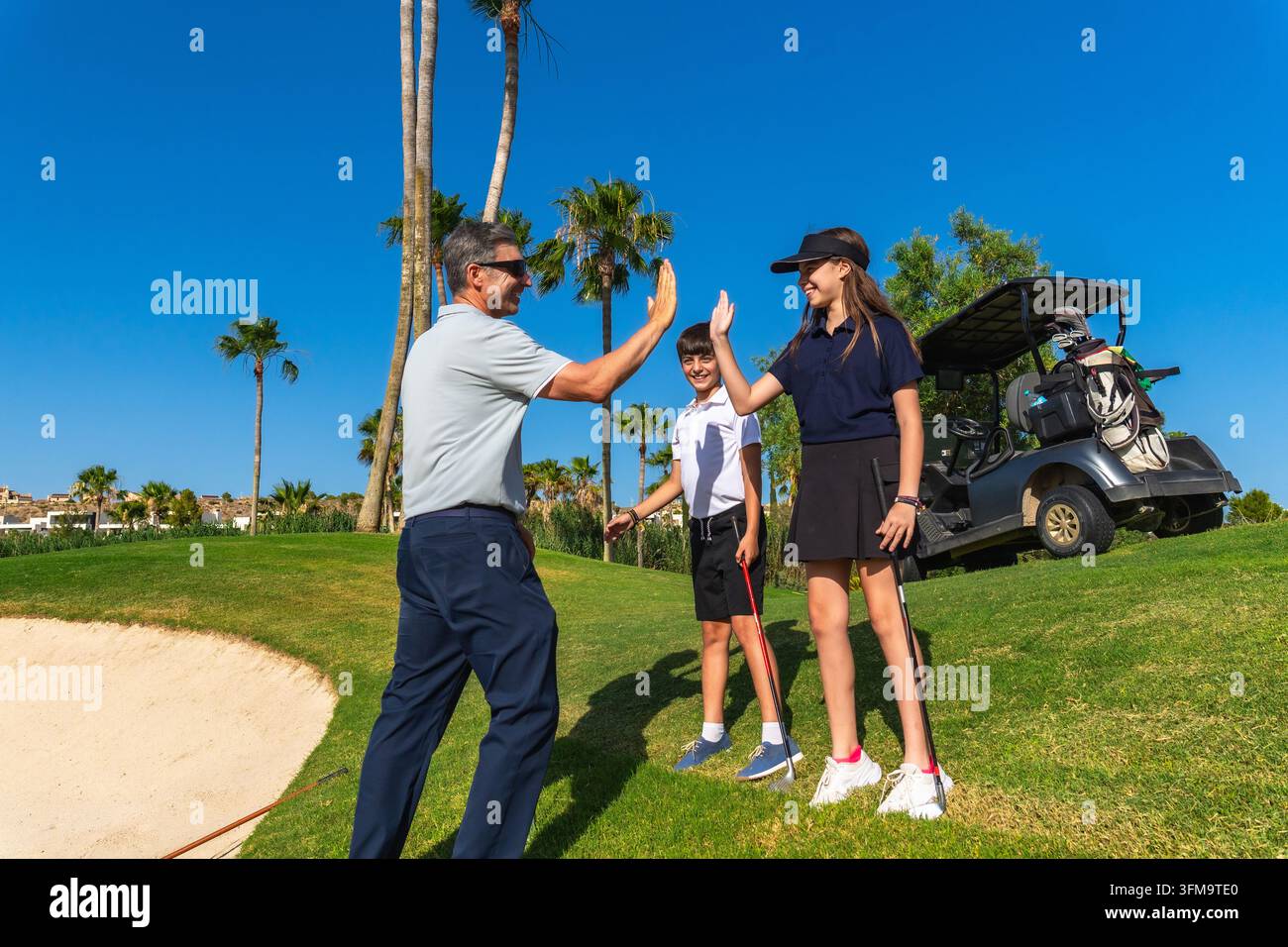 Golflehrer gibt Kindern nach einer erfolgreichen Stunde ein High Five Stockfoto