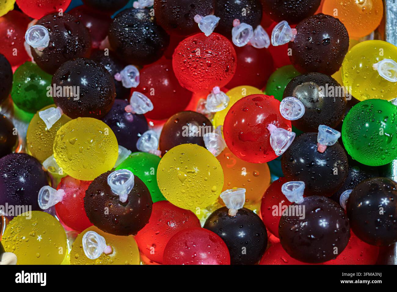 Bunte Fruchtgelee-Kugeln mit Wassertropfen, gestapelt in einem gekühlten Metalltablett an einem thailändischen Marktstand, runde Süßigkeiten in klaren Plastikballonpackungen Stockfoto