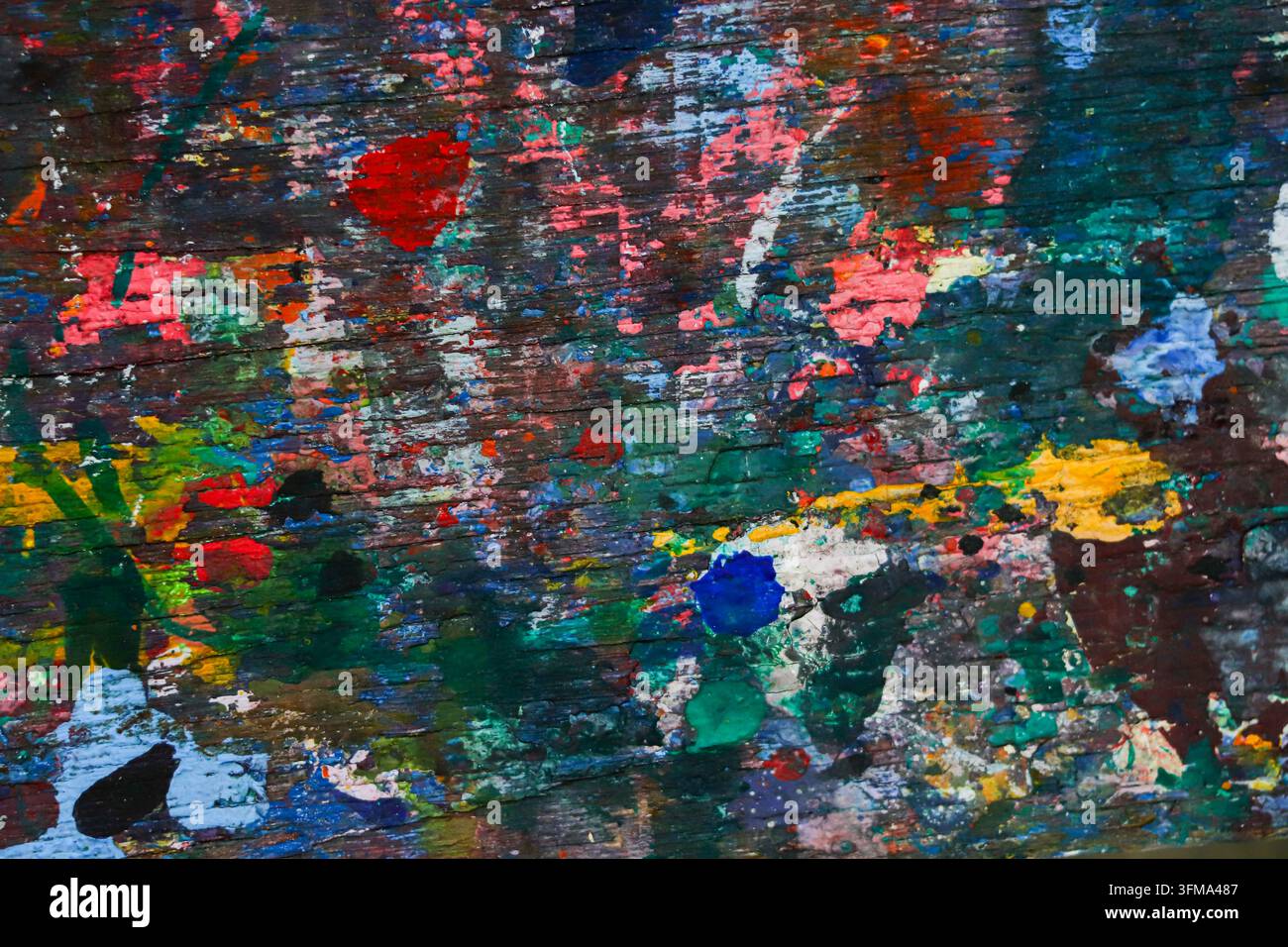 Nahaufnahme von mehrfarbigen getrockneten Acrylfarbspritzern und -flecken auf einer verwitterten Holzoberfläche eines Künstleratelier-Arbeits-tisches. Stockfoto