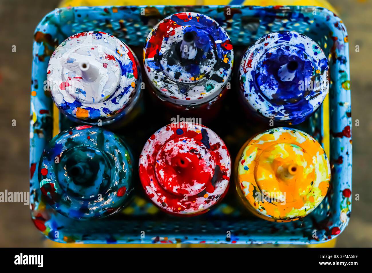 Sechs gebrauchte Kunstfarbflaschen mit mehrfarbigem Farbrest, angeordnet in einer blauen Plastikschale, von oben in Nahaufnahme fotografiert. Stockfoto