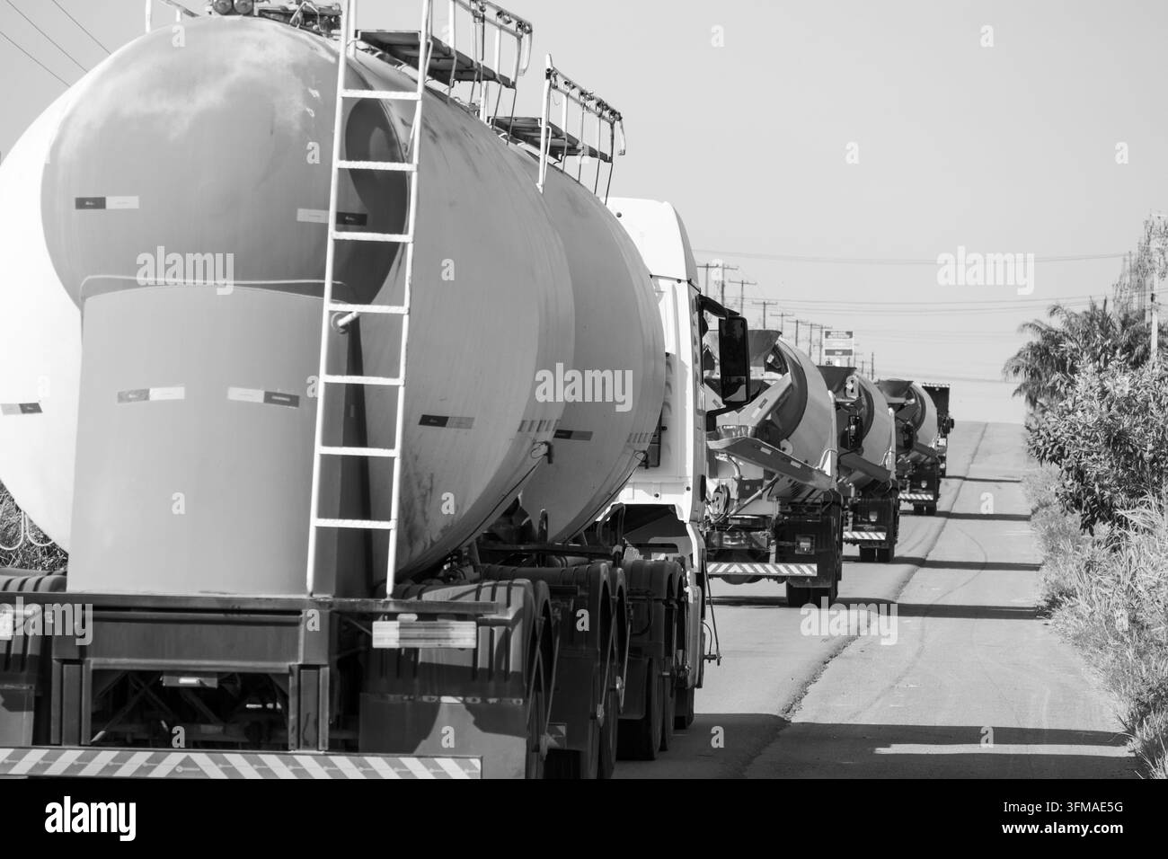 Monochrom-Studie des schweren Gütertransports, der einen Konvoi von Nutzfahrzeugen auf einer offenen Straße bildet. Stockfoto