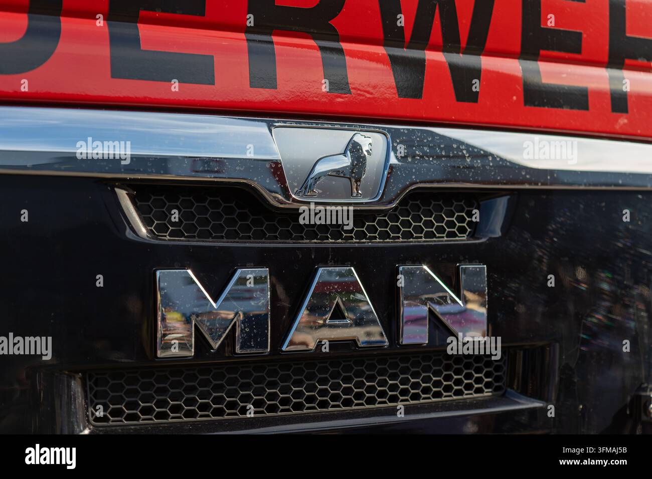 MAN-Markenlogo und Löwenemblem auf dem Kühlergrill eines Feuerwehrautos, das einen Teil der Fahrzeugbeschriftung zeigt Stockfoto