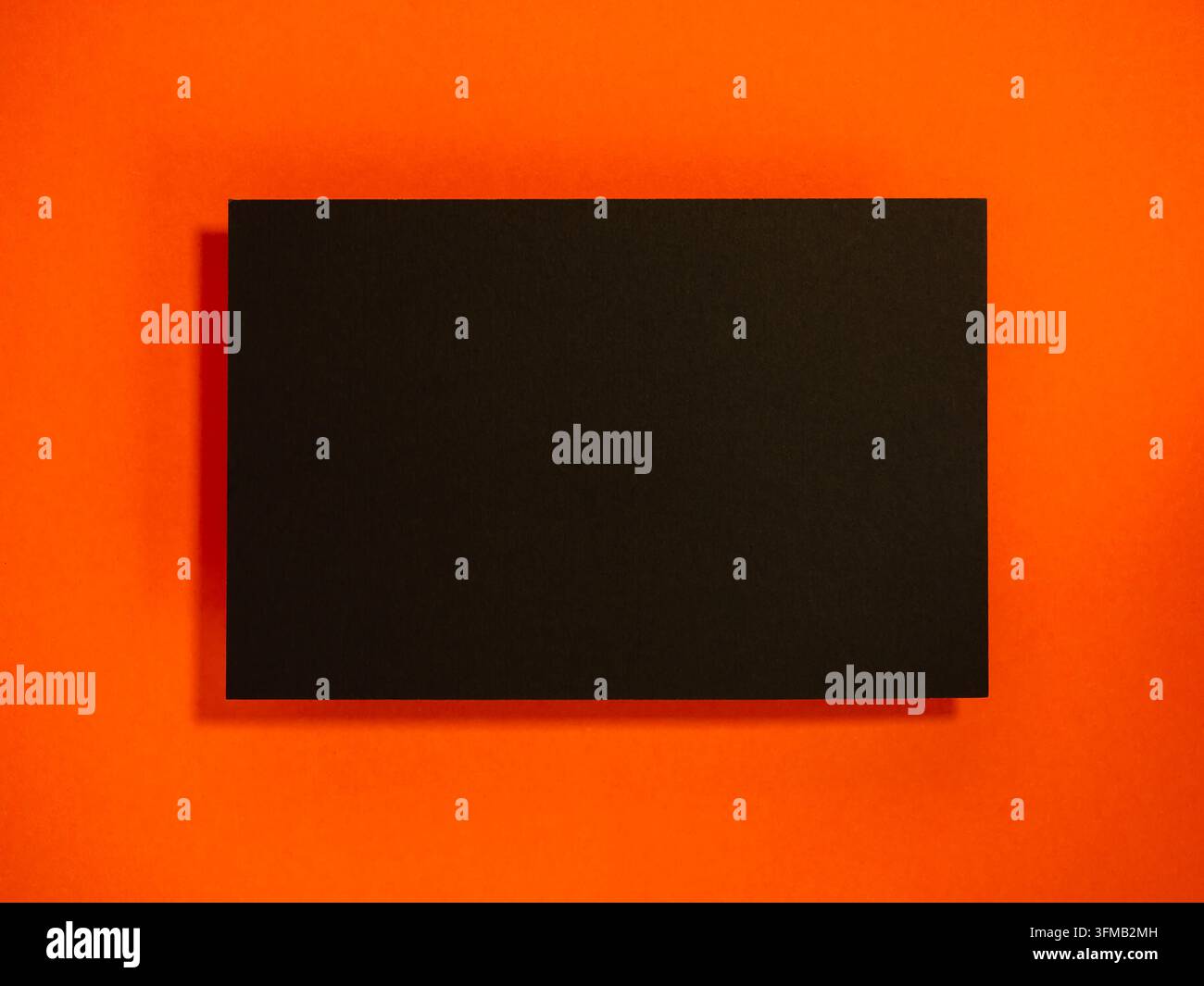 Leere schwarze Karte, die auf einem horizontalen, lebhaften orangefarbenen Hintergrund mit subtilen Schatten angezeigt wird, ideal für Premium-Branding, Visitenkarten-Design, Unternehmens-i Stockfoto