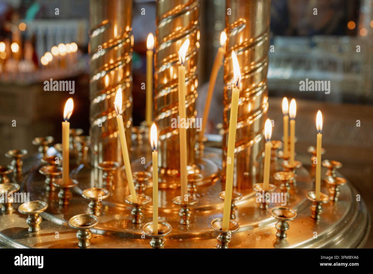 Nahaufnahme von beleuchteten Kerzen in einer friedlichen und ruhigen Umgebung, religiöse Darstellungen und zeremonielle Gegenstände, mit metallenen Kerzenständern und Wachs Stockfoto