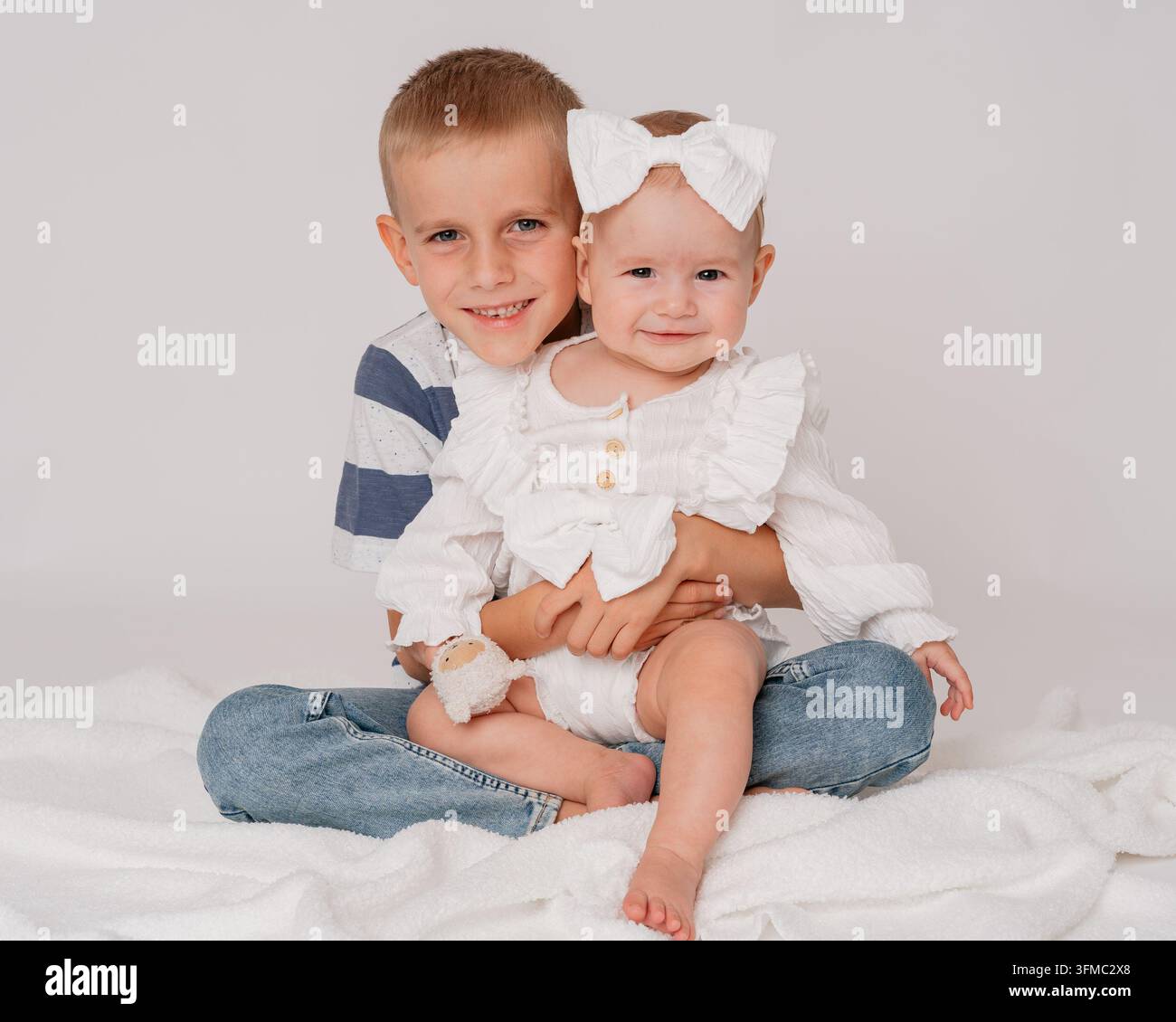 zwei entzückende Kinder, die sich herzlich in einem gemütlichen Indoor-Studio umarmen, umgeben von einer weichen Decke und einem plüschigen Stofftier, in einer Nahaufnahme des Auges aufgenommen Stockfoto