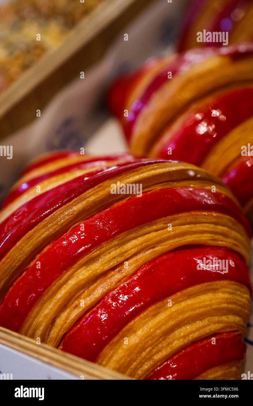 Französisches Himbeer-Croissant mit frischen Erdbeeren, mit knusprigen goldenen Schichten und glänzender roter Beerenfüllung, ausgestellt in einer Konditorei. Stockfoto